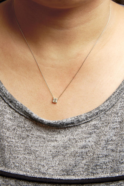 Close-up front view of a yellow metal necklace on a model featuring a small pendant with white gemstones in round and baguette shapes in prong and channel settings.