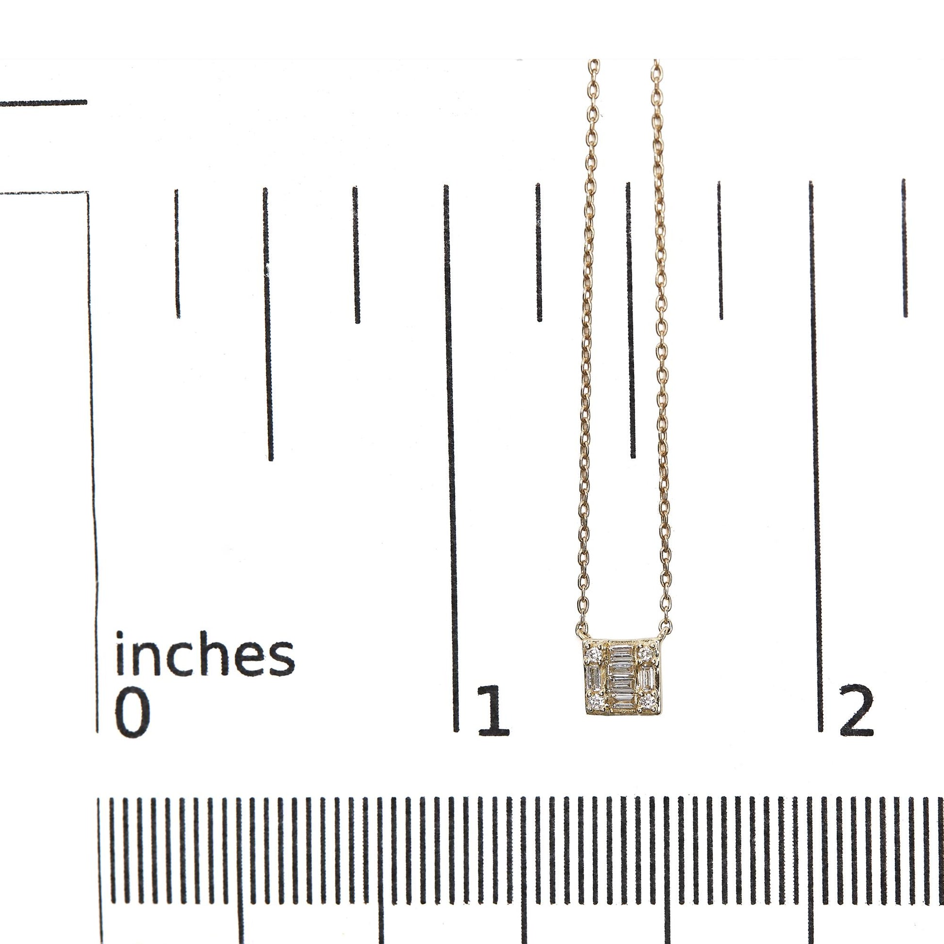 Close-up front view of a yellow metal necklace with a square pendant featuring white round and baguette-shaped gemstones in channel and prong settings, displayed on a ruler for size reference.