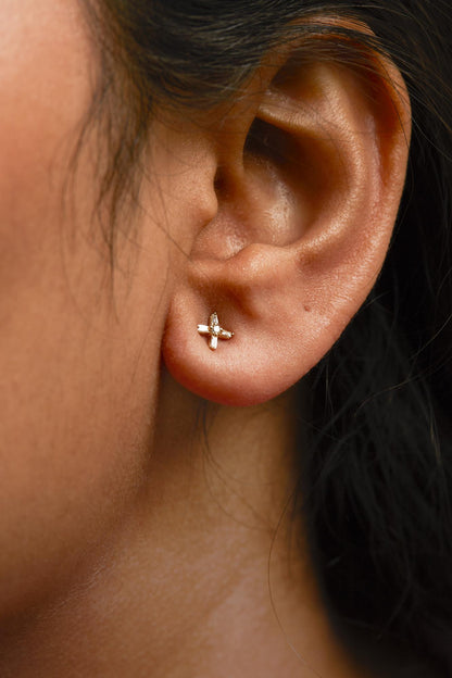 Close-up side view of a yellow metal earring on a model's ear featuring a small cluster design with round and baguette-shaped white gemstones in prong settings.