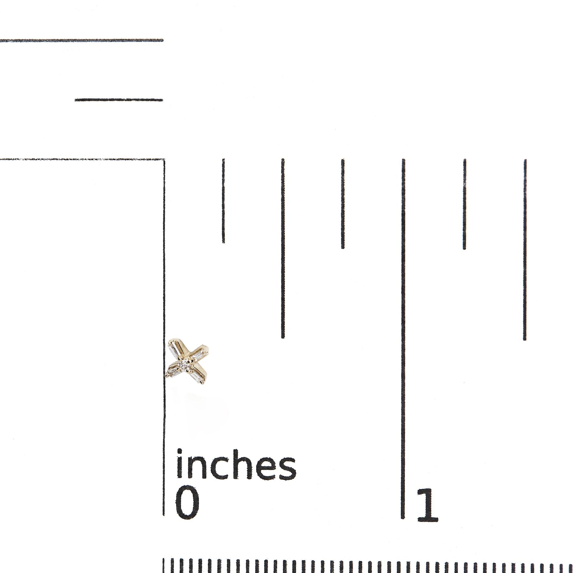 Close-up front view of a yellow metal earring with white round and baguette shaped gemstones in prong settings, placed on a ruler for size reference.