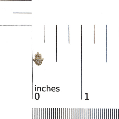 Close-up of a small yellow metal earring shaped like a hand with white gemstones in pave setting, placed on a ruler for size reference.