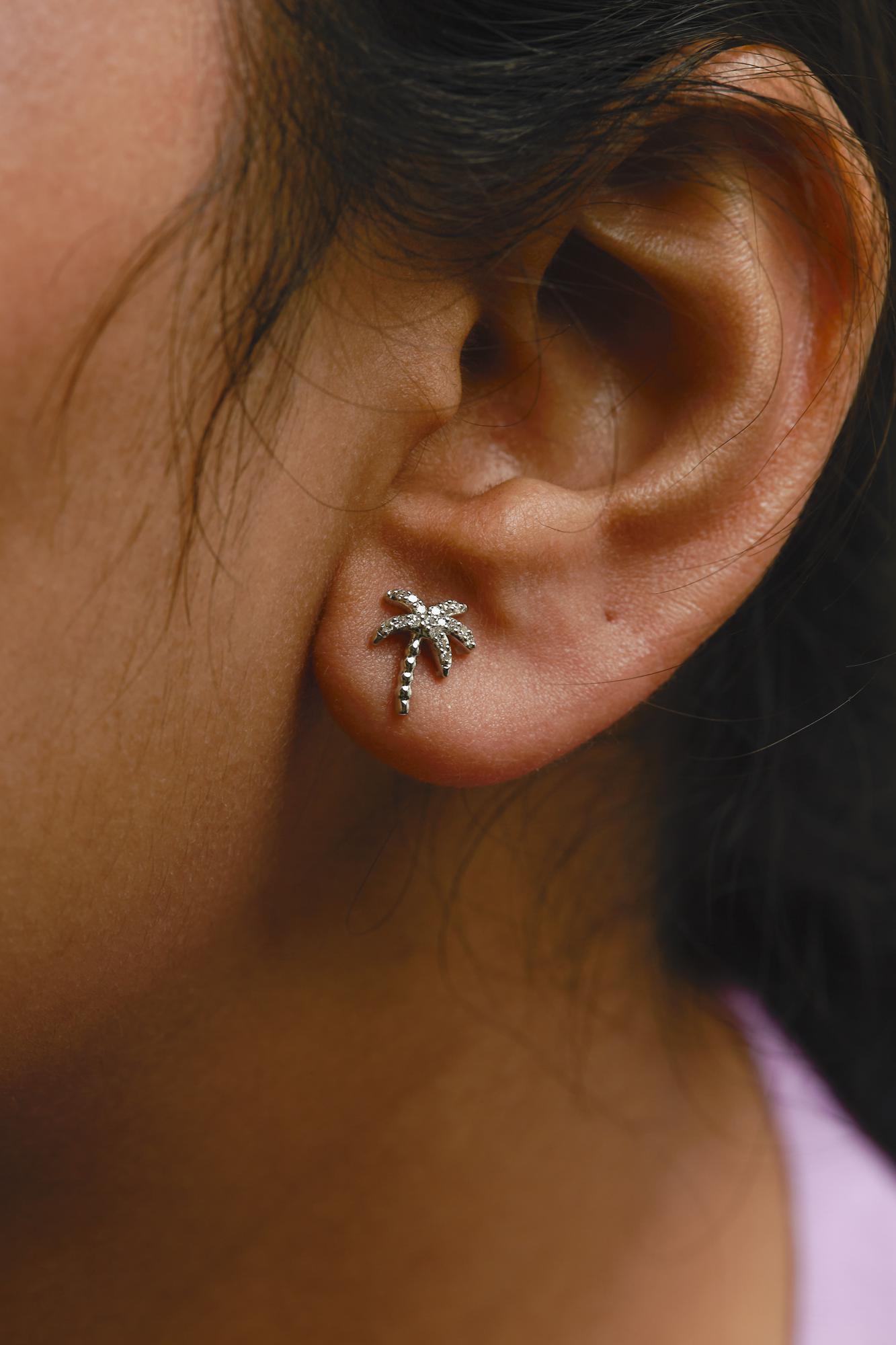 Close-up side view of a white metal palm tree-shaped earring with small round white gemstones in pave setting, worn on a model.