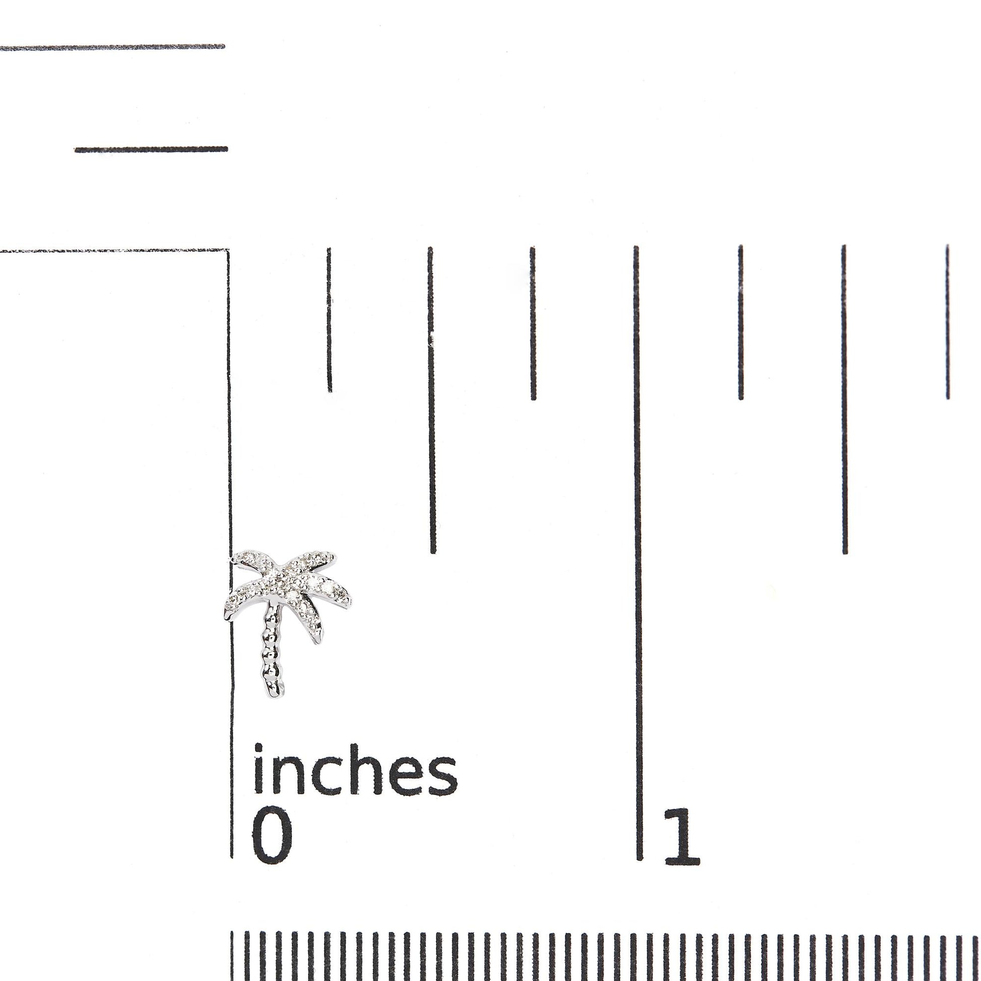 Close-up front view of a white metal palm tree-shaped earring with round white pave-set gemstones, placed on a ruler for size reference.