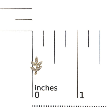 Close-up front angle of a yellow metal earring shaped like a small branch with multiple leaves paved with round white gemstones, placed on a ruler for size reference.