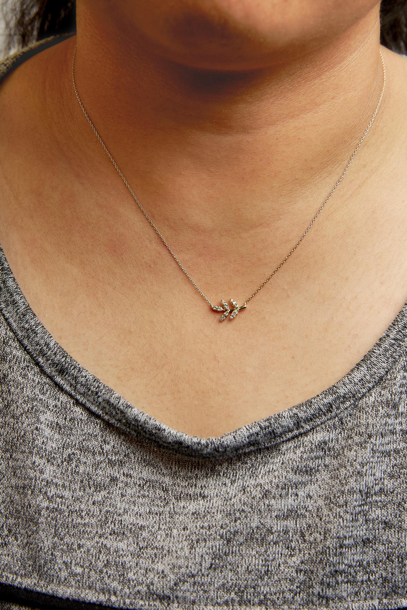 Close-up shot of a yellow metal necklace with a small leaf-shaped pendant set with white round pave gemstones, worn on a model.