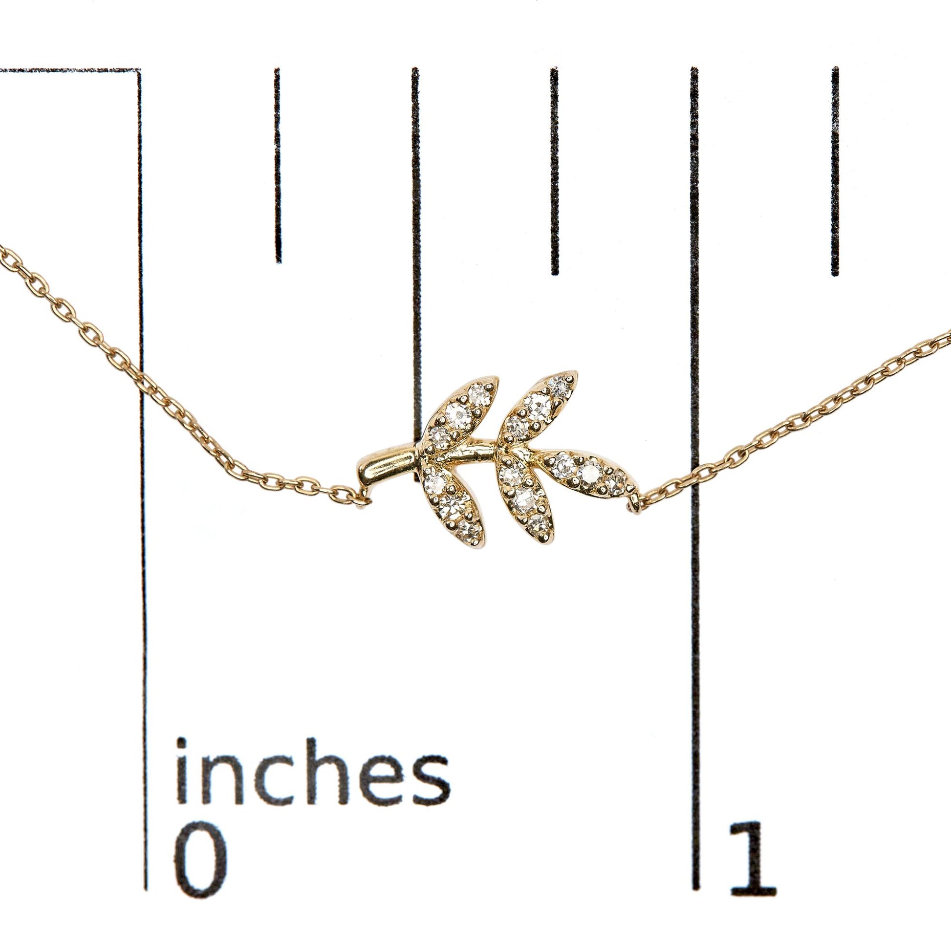 Close-up front view of a yellow metal necklace with a branch-shaped pendant adorned with small white round pave-set gemstones, displayed on a ruler for size reference.