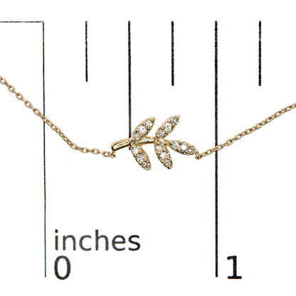 Close-up front view of a yellow metal necklace with a branch-shaped pendant adorned with small white round pave-set gemstones, displayed on a ruler for size reference.