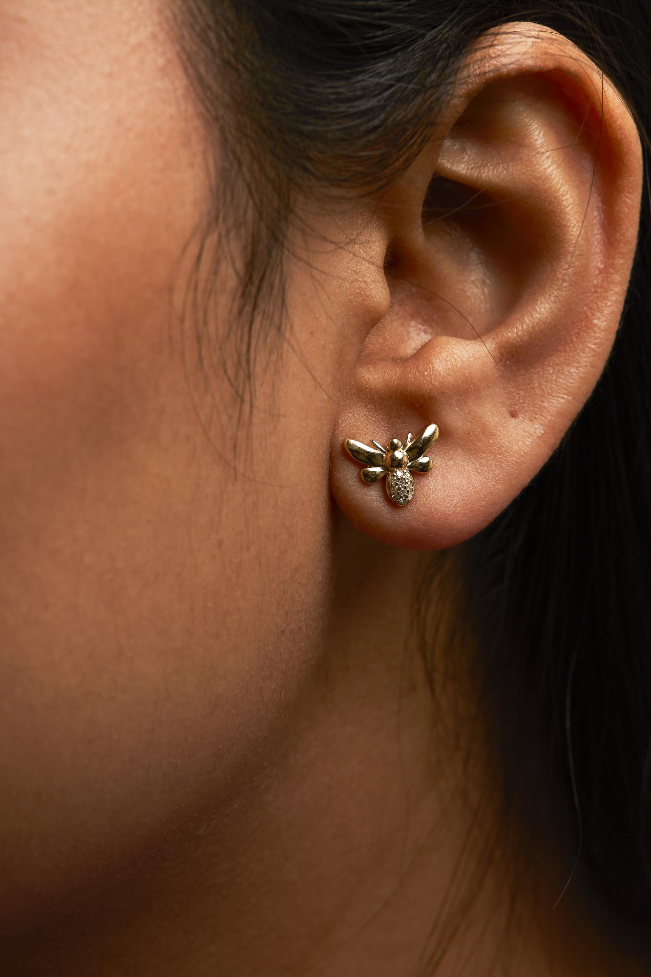 Close-up side view of a yellow metal bee-shaped earring with white round gemstones in a pave setting, worn on a model's ear.