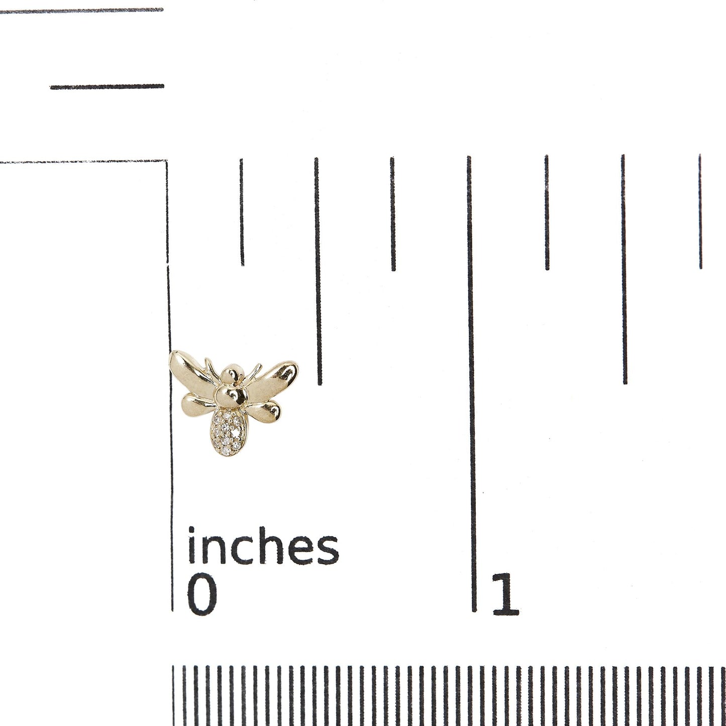 Close-up top view of a yellow metal bee-shaped earring with round white gemstones in pave setting, placed on a ruler for size reference.