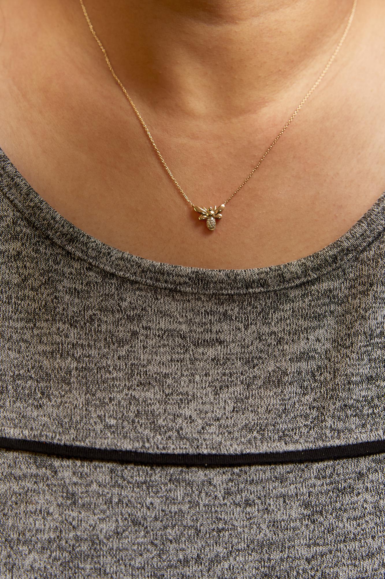 Close-up front view of a yellow metal necklace with a small bee-shaped pendant featuring white round pave-set gemstones, worn on a model.