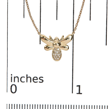 Close-up of a yellow metal bee-shaped necklace pendant with white round pave-set gemstones on its lower body, shown on a ruler for size reference.
