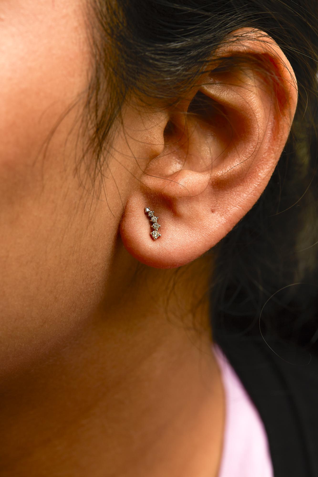Close-up side view of a model wearing a white metal earring featuring a vertical curve of multiple prong-set round white gemstones.
