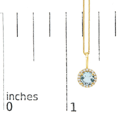 Yellow metal necklace with a round blue gemstone pendant surrounded by small white gemstones, shown hanging on a scale at a slight angle.
