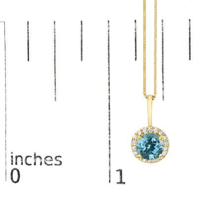Yellow metal necklace with a round blue gemstone pendant surrounded by small white gemstones, shown on a scale from a front angle.