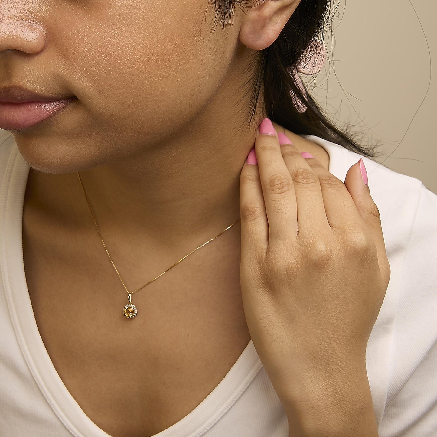 Yellow metal necklace with a round orange gemstone center surrounded by small white gemstones in a shared prong setting, shown worn on a model from a front angle.