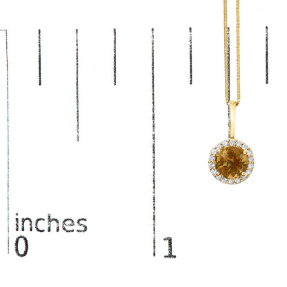 Yellow metal necklace with a round orange gemstone pendant surrounded by small white gemstones, shown on a scale from a front angle.