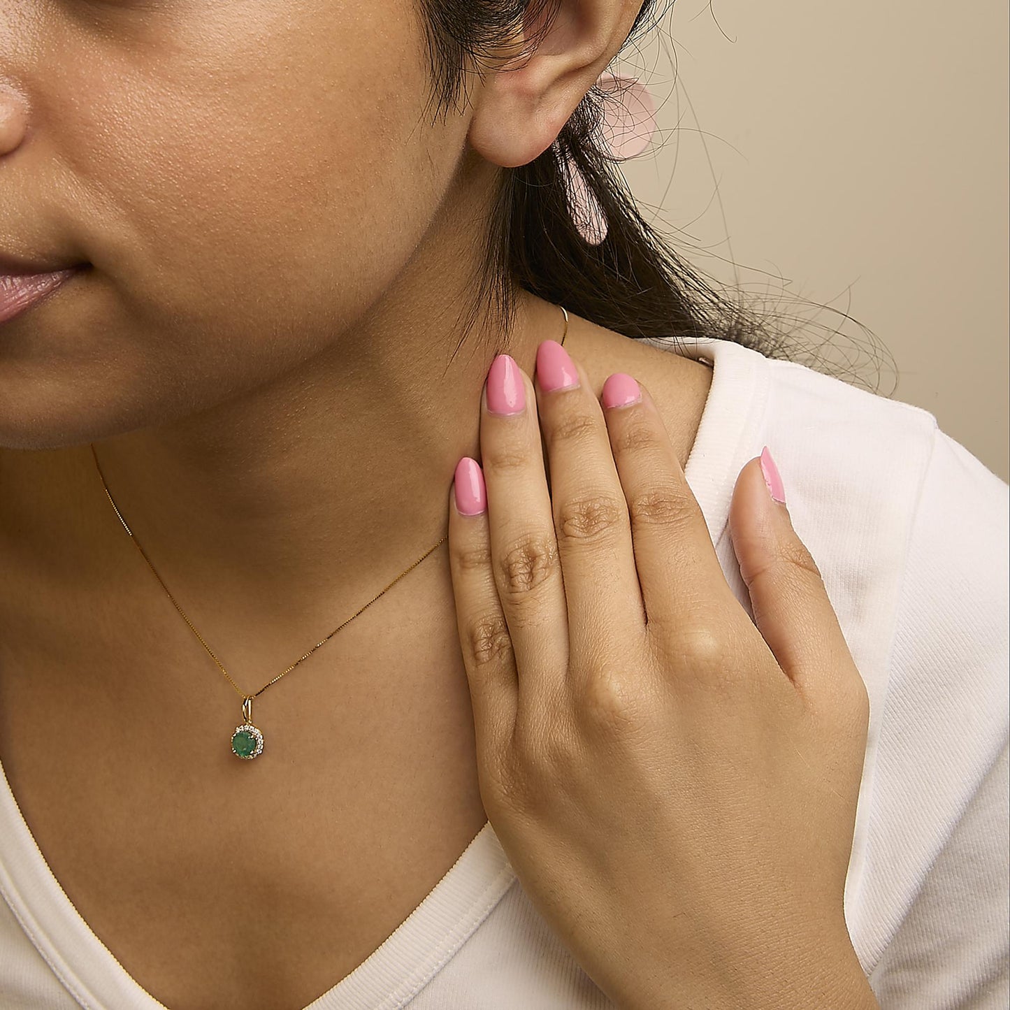 Yellow metal necklace with a round green gemstone pendant surrounded by white gemstones, shown worn on a model from the front angle.
