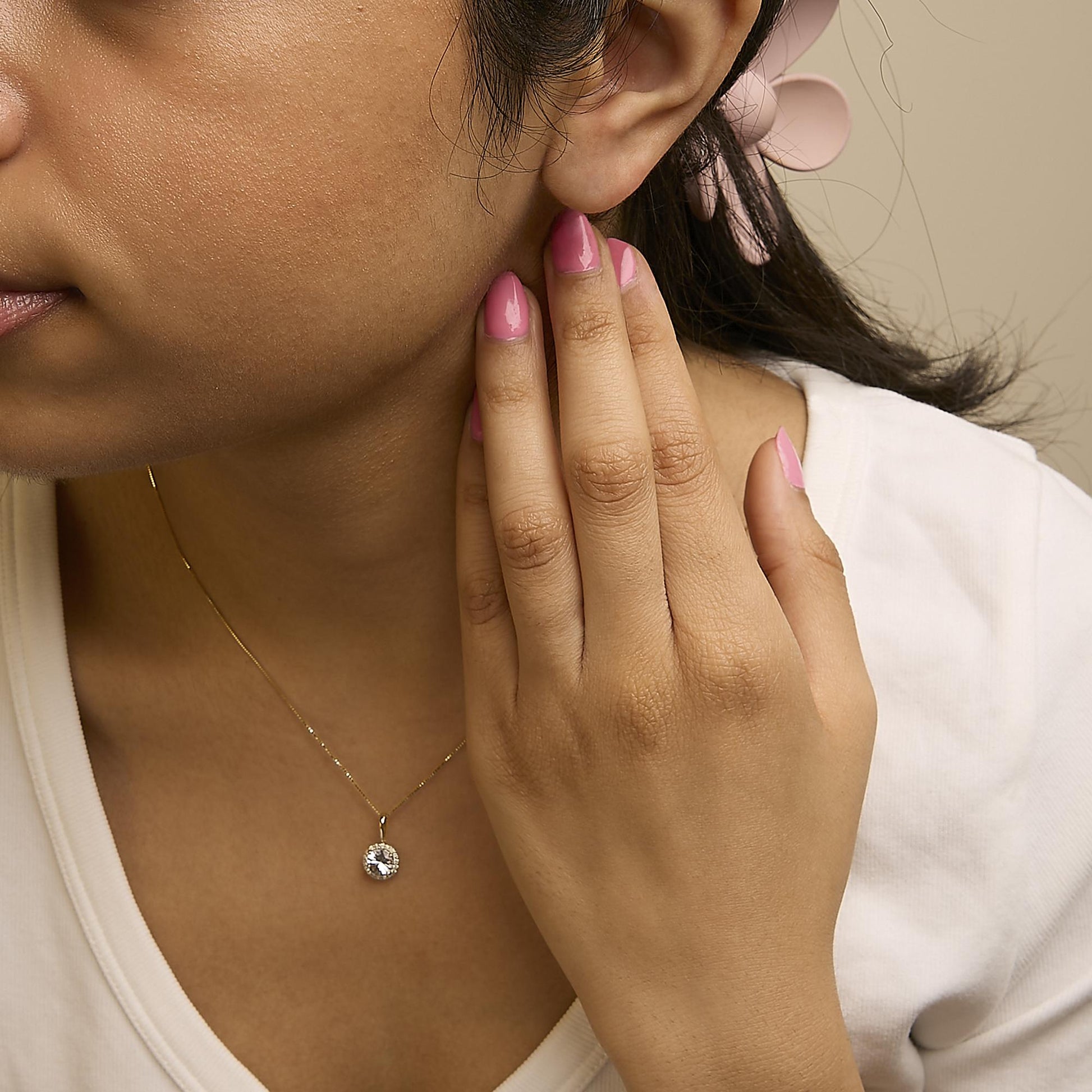 Yellow metal necklace with a round white gemstone pendant surrounded by smaller round white gemstones, shown worn on a model in a close-up angled view.