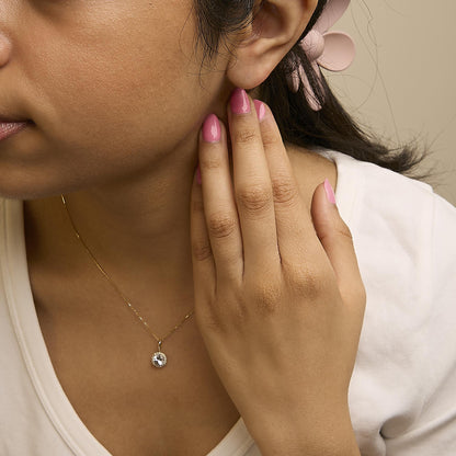 Yellow metal necklace with a round white gemstone pendant surrounded by smaller round white gemstones, shown worn on a model in a close-up angled view.