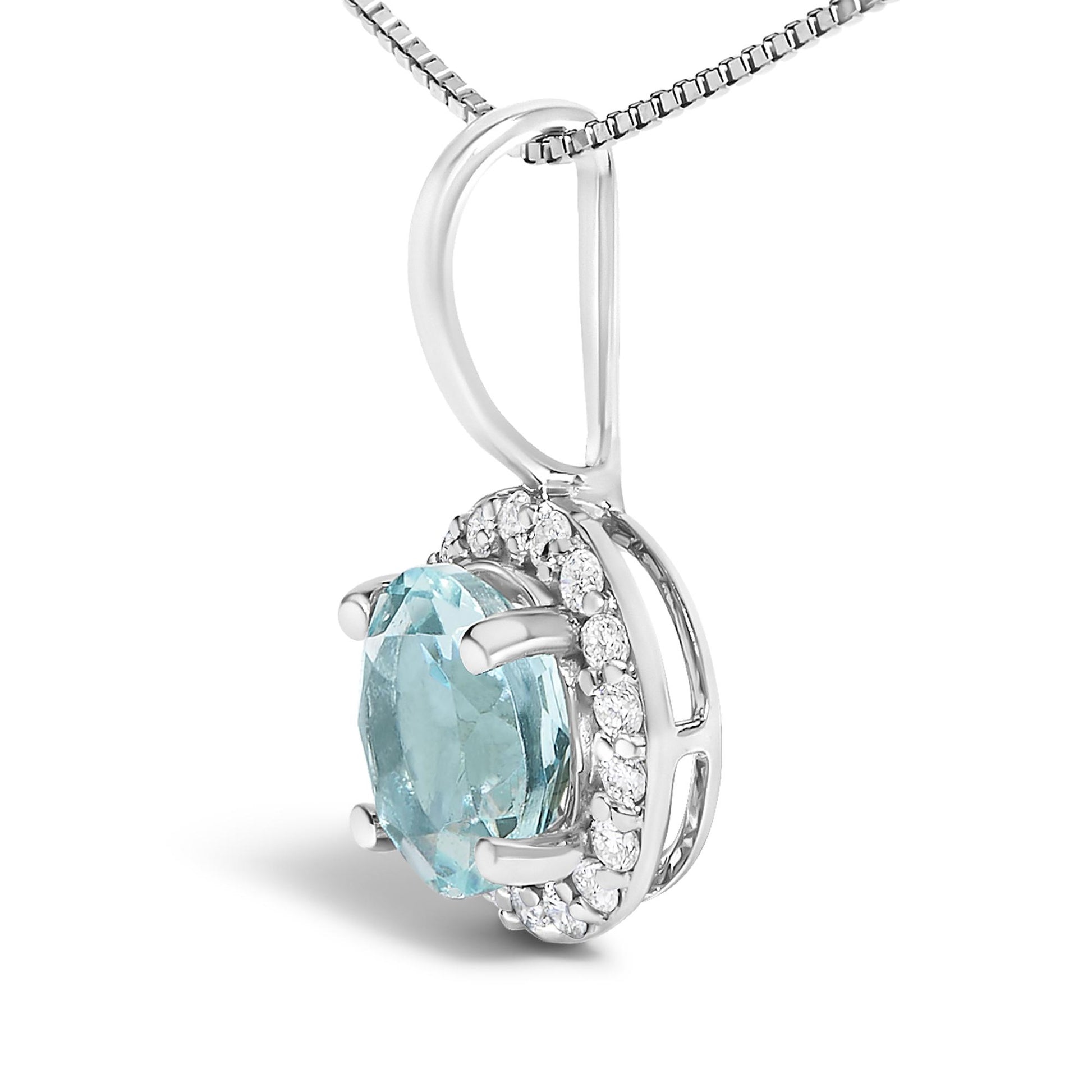 Close-up front angle view of a white metal necklace pendant featuring a round blue gemstone set with four prongs, surrounded by a halo of round white gemstones in a shared prong setting. The necklace chain is partially visible threaded through the pendant's bail.