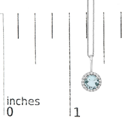 White metal necklace with a round blue gemstone center surrounded by small white gemstones, shown hanging on a ruler scale from a top-front angle.
