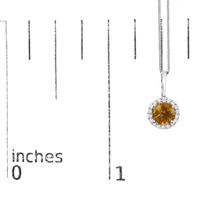 Close-up front view of a white metal necklace pendant with a round orange gemstone center, surrounded by a circular halo of small round white gemstones, shown on a ruler scale.