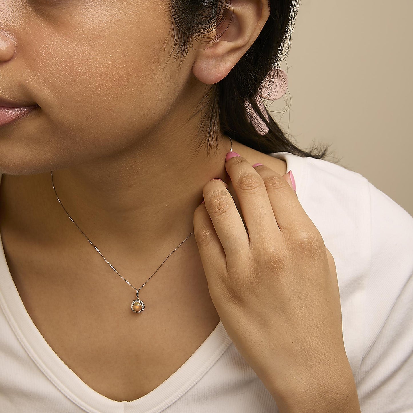 Close-up front angle of a model wearing a white metal necklace with a round multi-color gemstone pendant surrounded by small round white gemstones in shared prong settings.