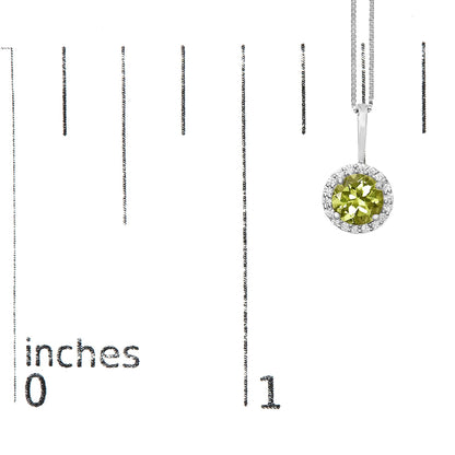 White metal necklace with a round green gemstone pendant surrounded by round white gemstones in a shared prong setting, shown on a scale from a front angle.
