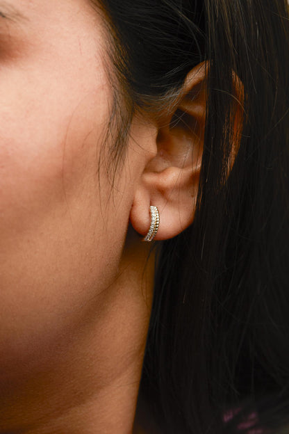 Close-up side view of a yellow metal earring with two rows, one plain and one with white round pave-set gemstones, worn on a model's ear.