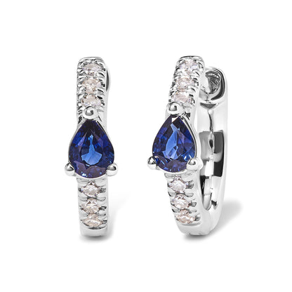 Front angle view of white metal hoop earrings with round pave-set white gemstones along the hoop and a pear-shaped blue gemstone in a three-prong setting at the center.