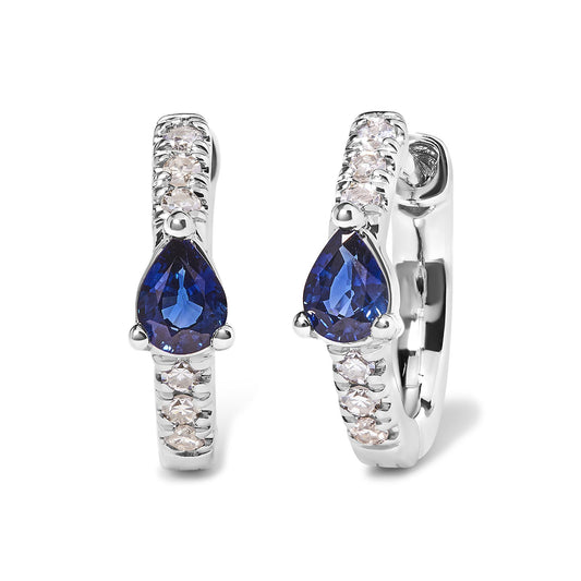 Front angle view of white metal hoop earrings with round pave-set white gemstones along the hoop and a pear-shaped blue gemstone in a three-prong setting at the center.