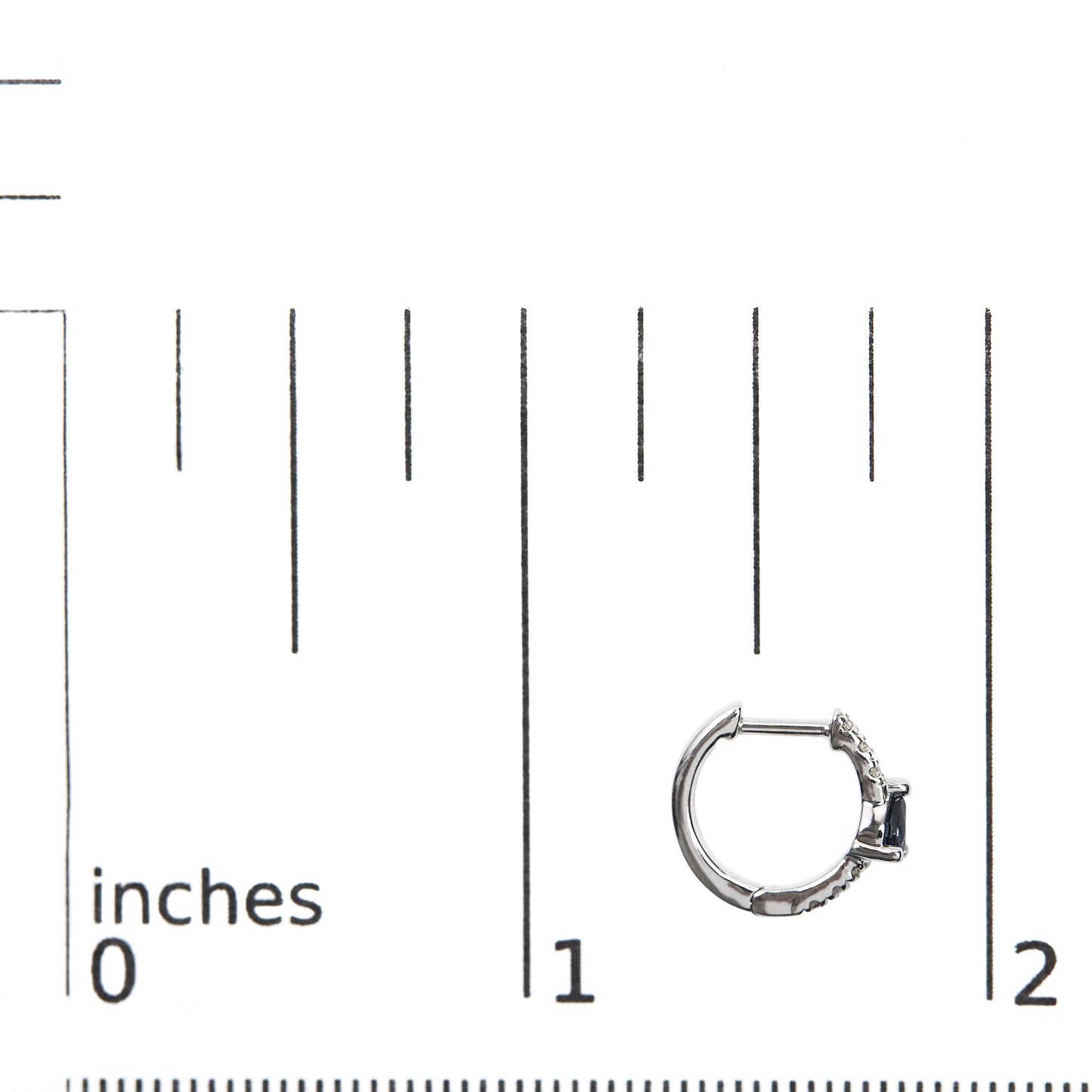 Close-up side angle of a white hoop earring placed on a ruler for size reference, featuring small round white gemstones in pave setting and a pear-shaped blue gemstone in a prong setting.