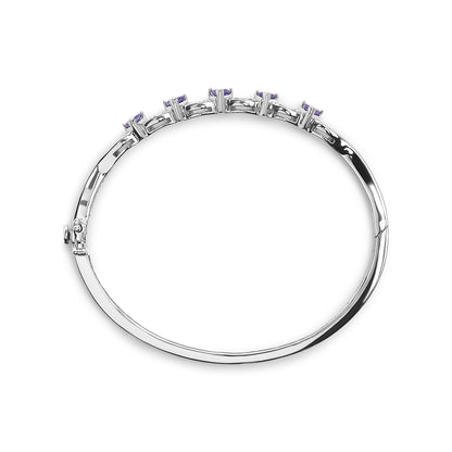 Top-down angle of a white metal bracelet with a row of white baguette-shaped gemstones in channel setting and blue trillion-shaped gemstones in three-prong setting.