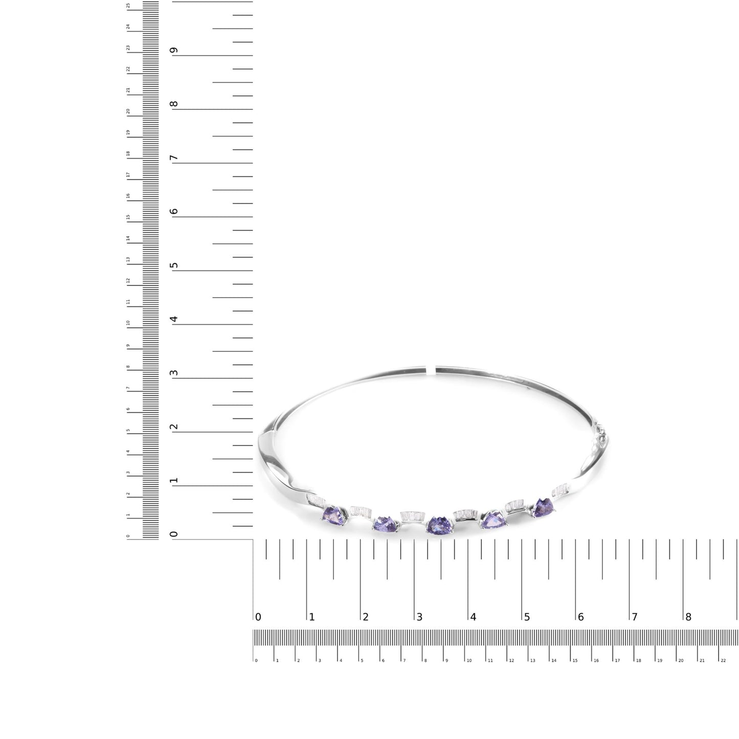 White metal bracelet with alternating blue trillion-shaped gemstones in prong settings and white baguette-shaped gemstones in channel settings, shown on a scale from a slightly elevated angle.