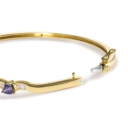 Close-up angled view of an open yellow bracelet featuring white baguette-shaped gemstones in a channel setting and a single blue trillion-shaped gemstone in a three-prong setting near the clasp.