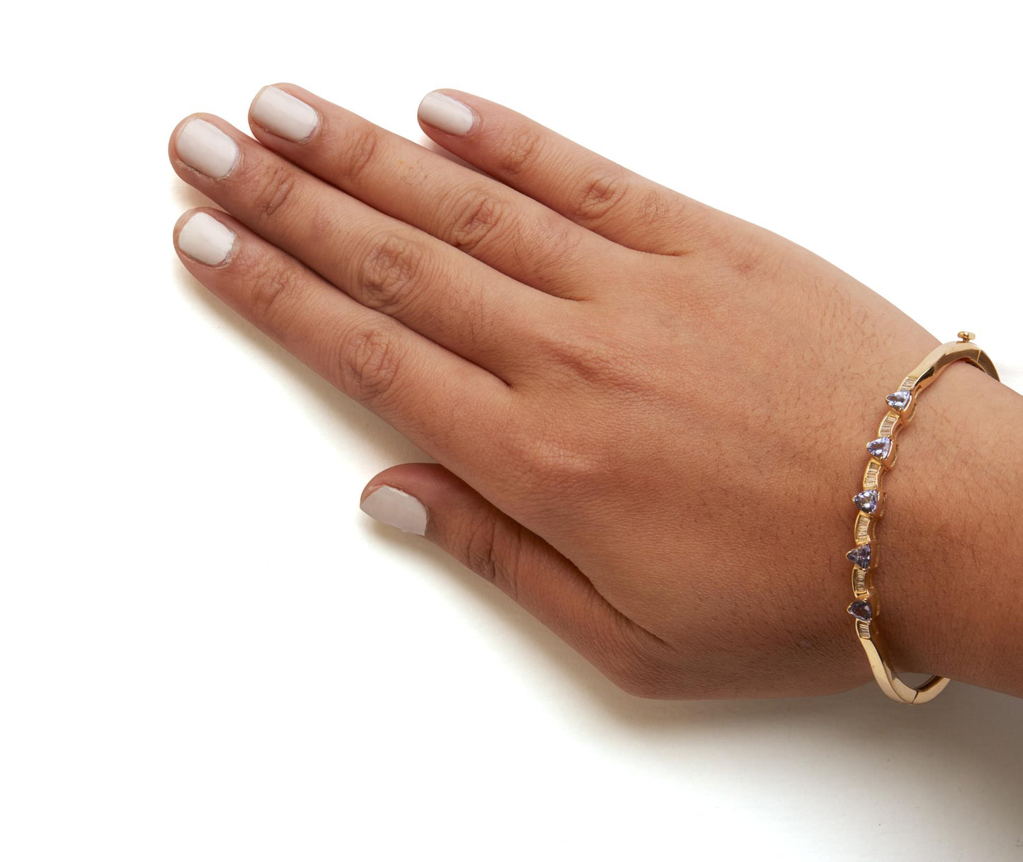 Yellow bracelet with white baguette-shaped gemstones in a channel setting and blue trillion-shaped gemstones in a prong setting, shown worn on a model's wrist from a top angle.