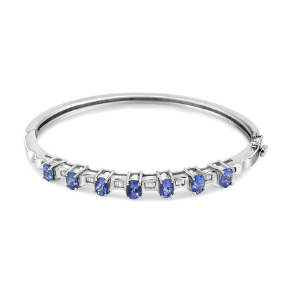 White metal bracelet with seven blue oval gemstones in prong settings and small white baguette gemstones in channel settings, shown from a front angle.