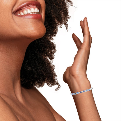 White metal bracelet with alternating channel-set white baguette-shaped gemstones and prong-set blue oval-shaped gemstones, shown on a model’s wrist from a side angle.