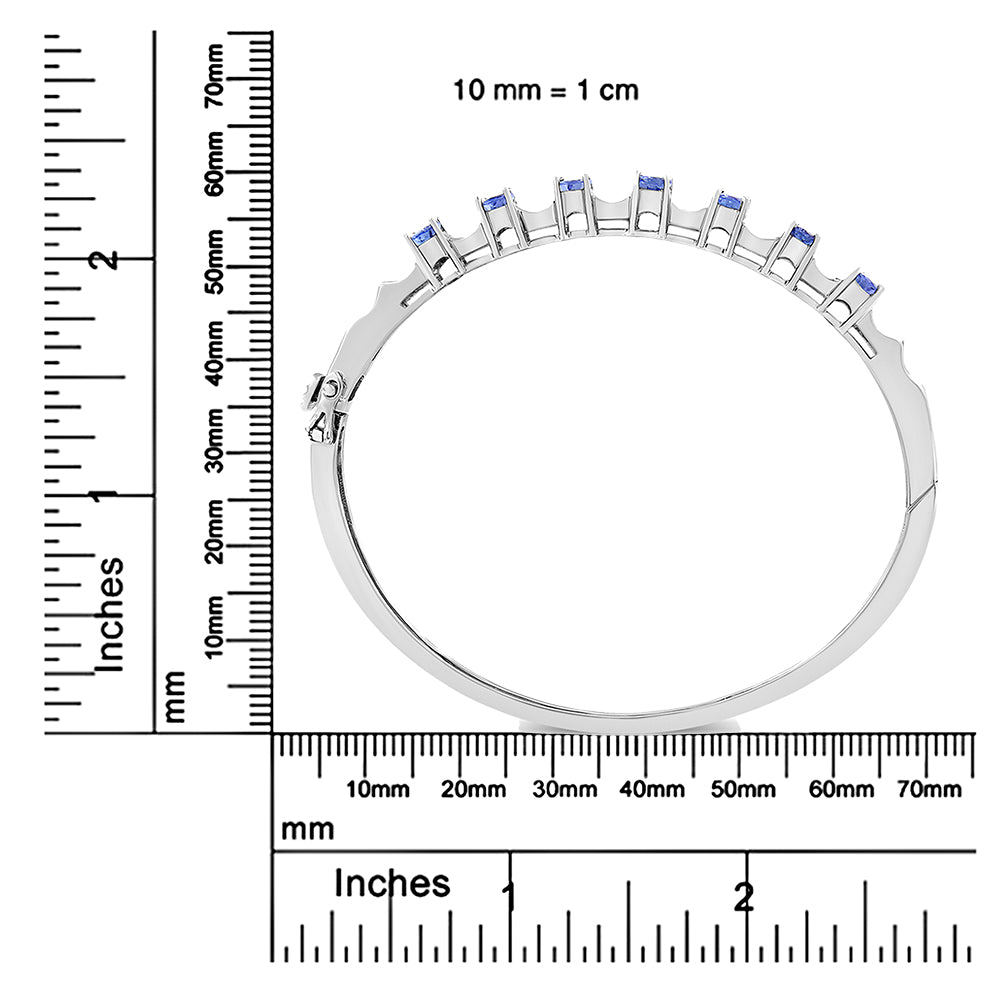 White metal bracelet with aligned blue oval gemstones set in prong settings along the top edge, shown from the side and placed on rulers for size reference.