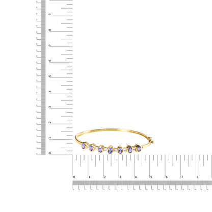 Yellow metal bracelet with oval purple gemstones in bezel settings, shown on a scale, photographed from the front angle.
