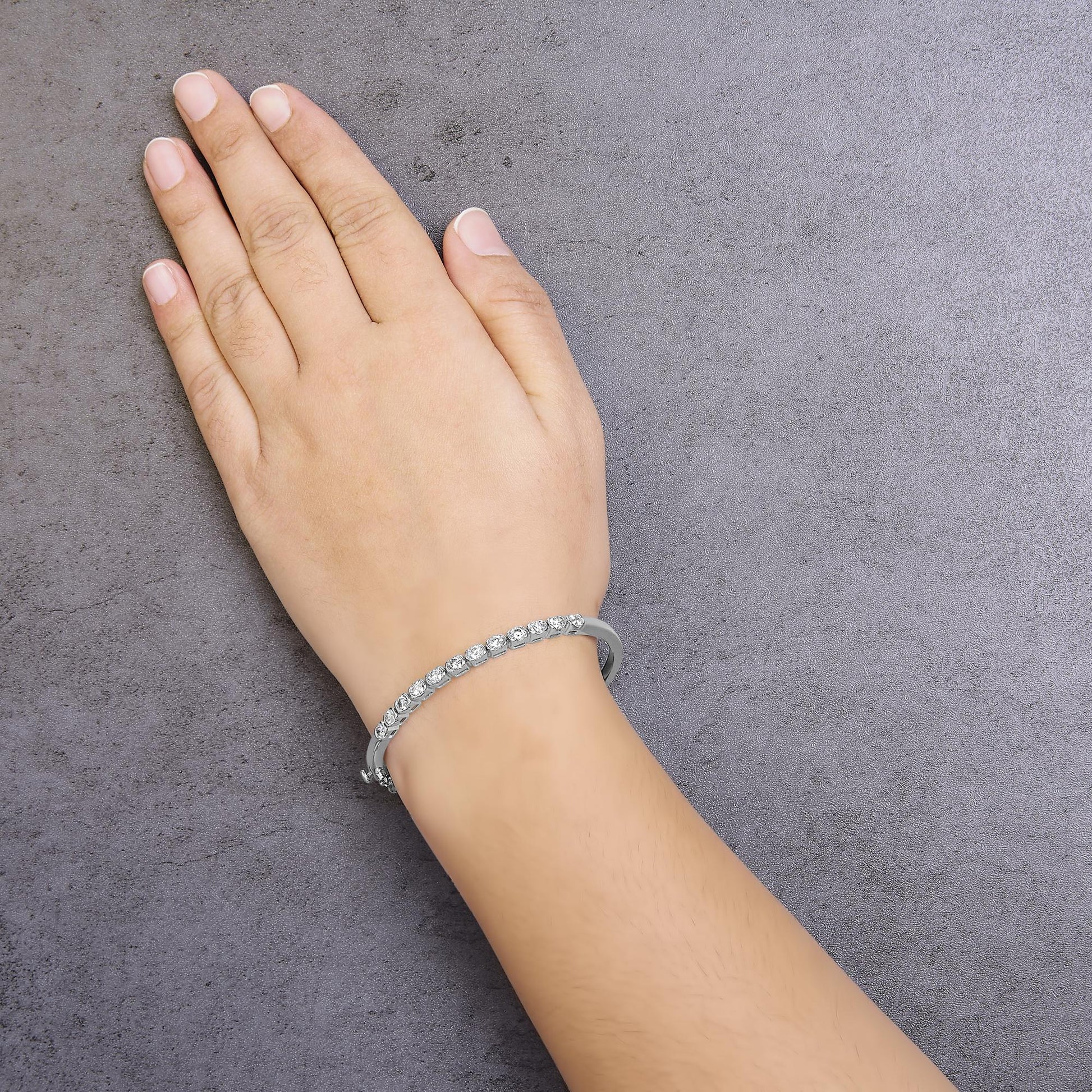 White metal bracelet with round white gemstones in pave setting, shown on a model's wrist, angled top-down.