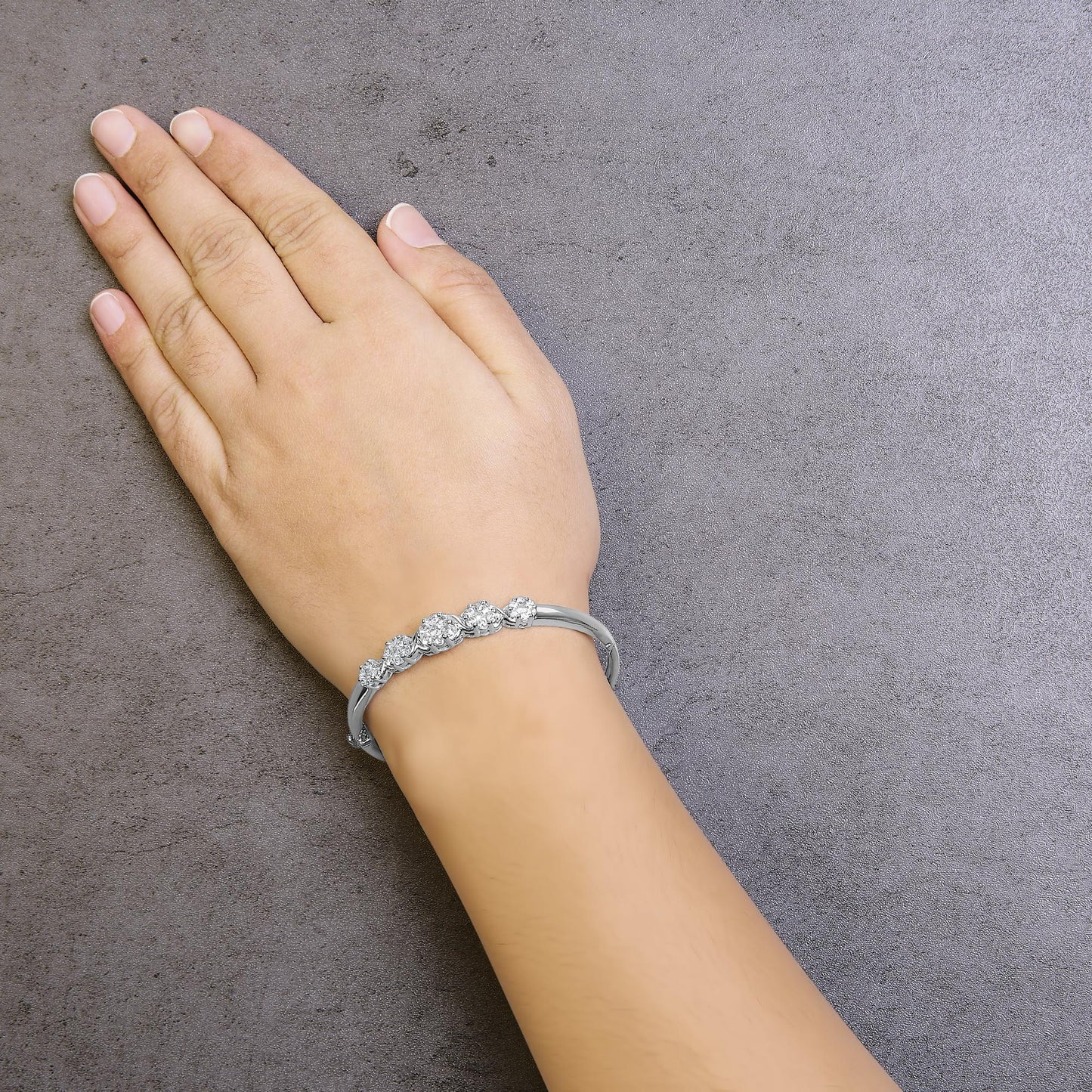 White metal bracelet with round prong-set white gemstones, shown on a model's wrist, top-down angle.