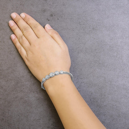 White metal bracelet with round prong-set white gemstones, shown on a model's wrist, top-down angle.