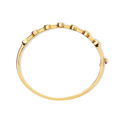 Top-down view of a yellow bracelet with round white gemstones set in a channel and oval blue gemstones in bezel settings along the top.