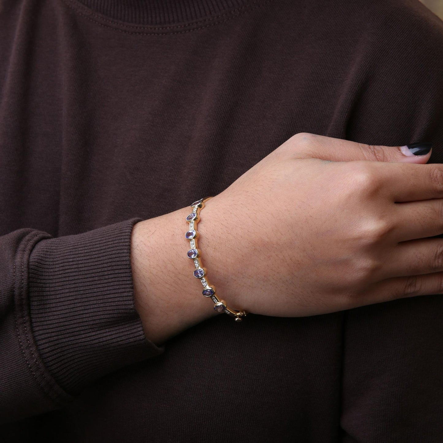 Yellow metal bracelet with oval blue gemstones in bezel setting and round white gemstones in channel setting, shown on a model's wrist from a side angle.
