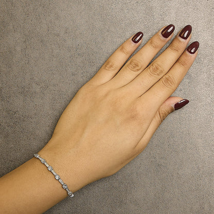 White metal bracelet with round white gemstones in miracle and prong settings, shown on a model's wrist from a top-down angle.