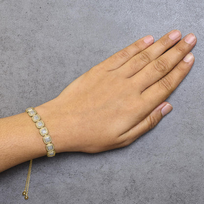 Yellow metal bracelet with square-shaped links featuring white gemstones in prong settings, worn on a model's wrist, side top-down angle.