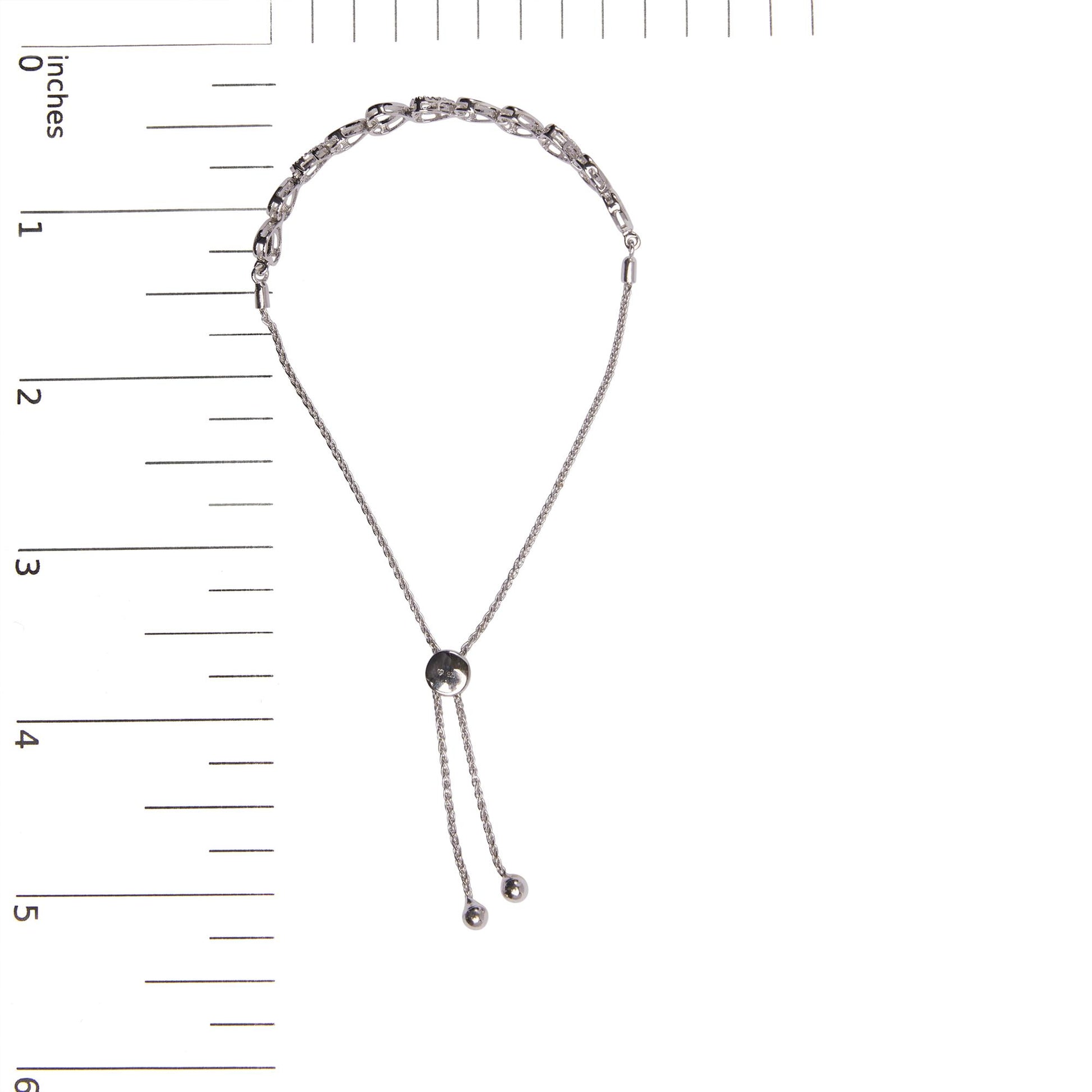 Top down view of white metal bracelet with two styles of round white gemstones in prong settings, shown on a ruler for size reference.