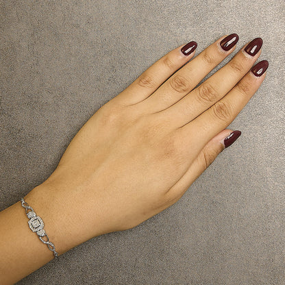 Close-up top view of a hand wearing a white metal bracelet with round white gemstones in a pave setting.