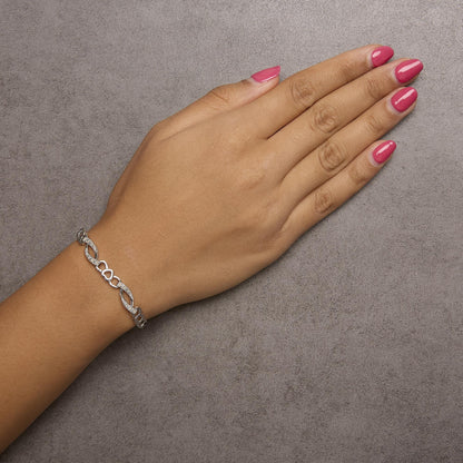 White metal bracelet with alternating loop and heart-shaped links, each loop set with white round gemstones in prong settings, shown on a model's wrist from above.